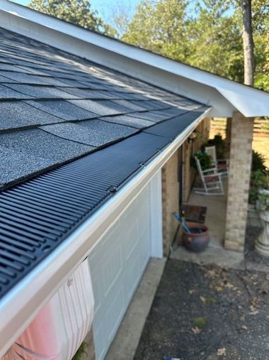 A gutter guard installed on a house's roof. Black guard, gray shingles, and beige trim.