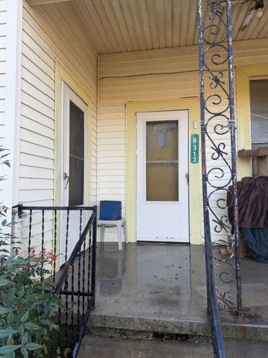 Yellow house porch with white door, black railing, and decorative iron column.
