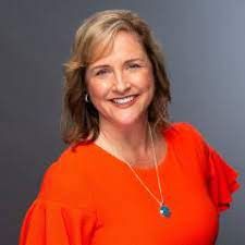 A woman in a red shirt and necklace is smiling for the camera.