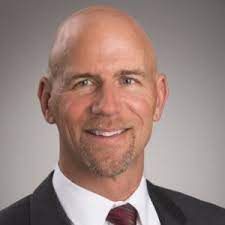 A bald man in a suit and tie is smiling for the camera.