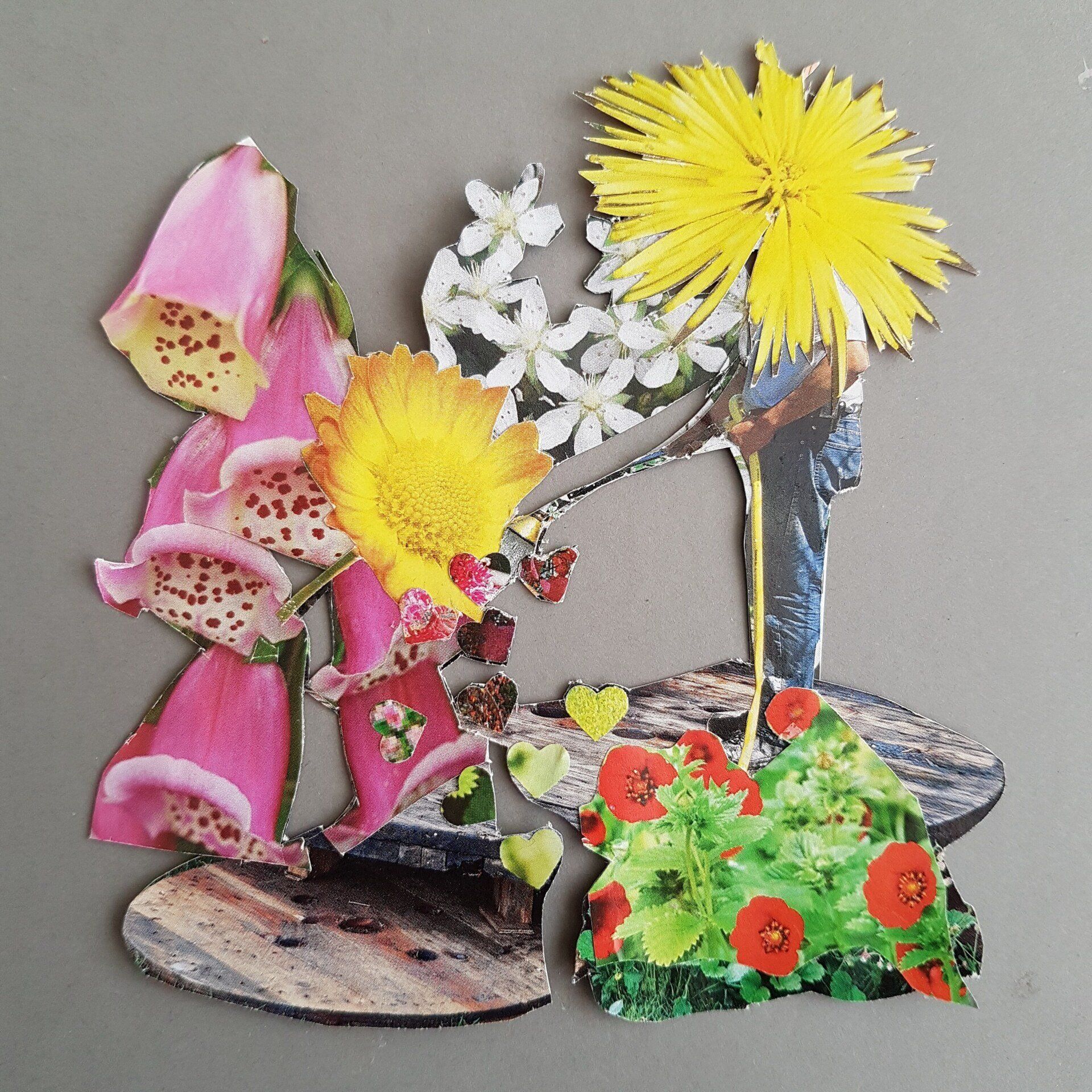 Bloemencollage van uitgeknipt papier met roze, gele en witte bloemen op een grijze achtergrond.