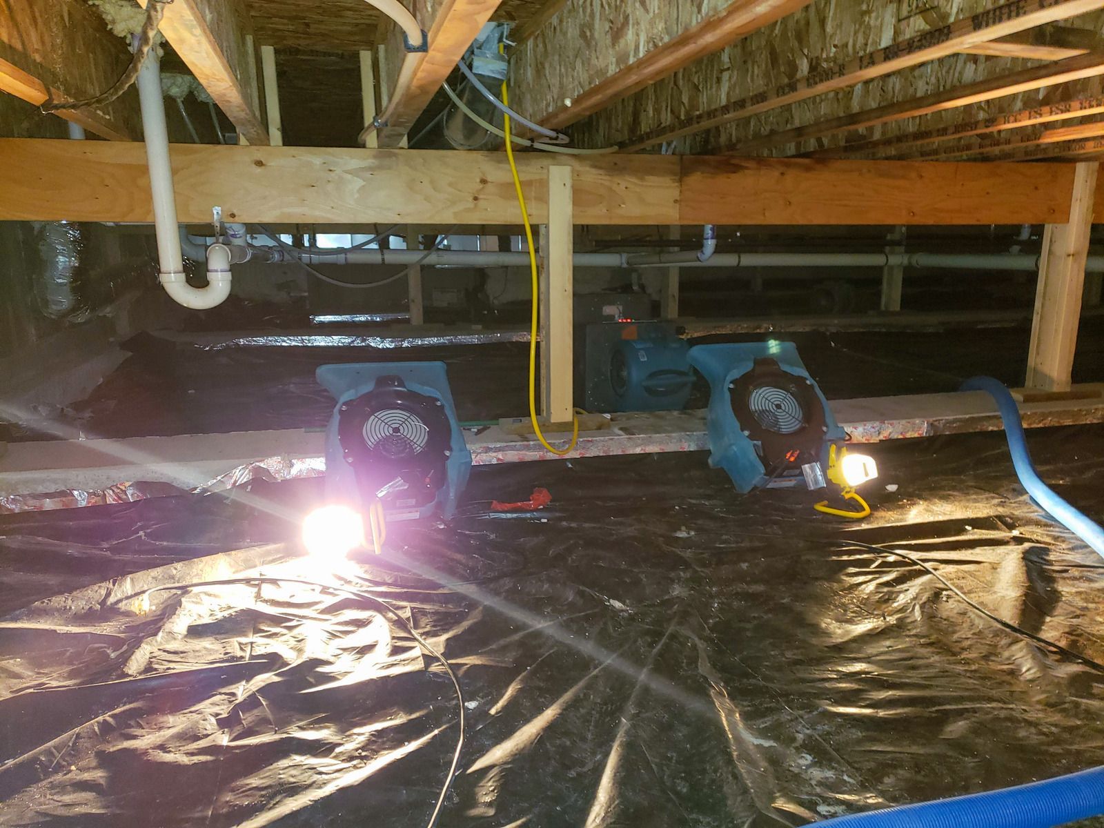 A couple of fans are sitting under a ceiling in a basement.
