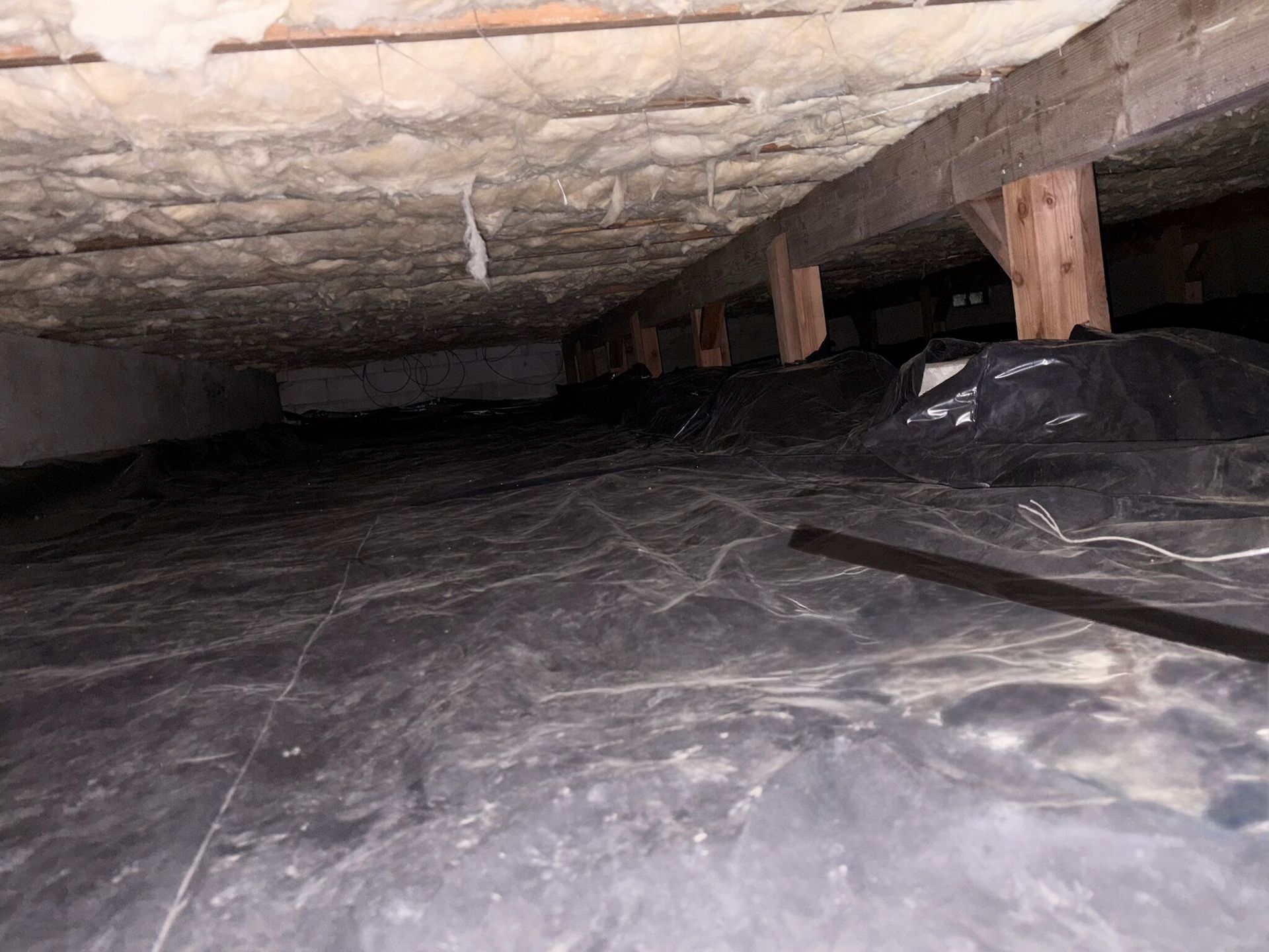 Underneath house: black plastic ground cover, wooden beams, insulation overhead.
