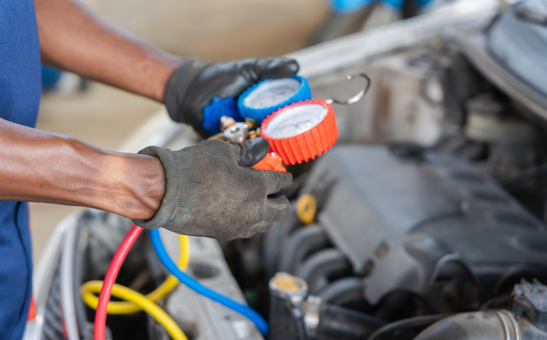 Mechanic using gauges to service a car engine, with colorful hoses connected nearby