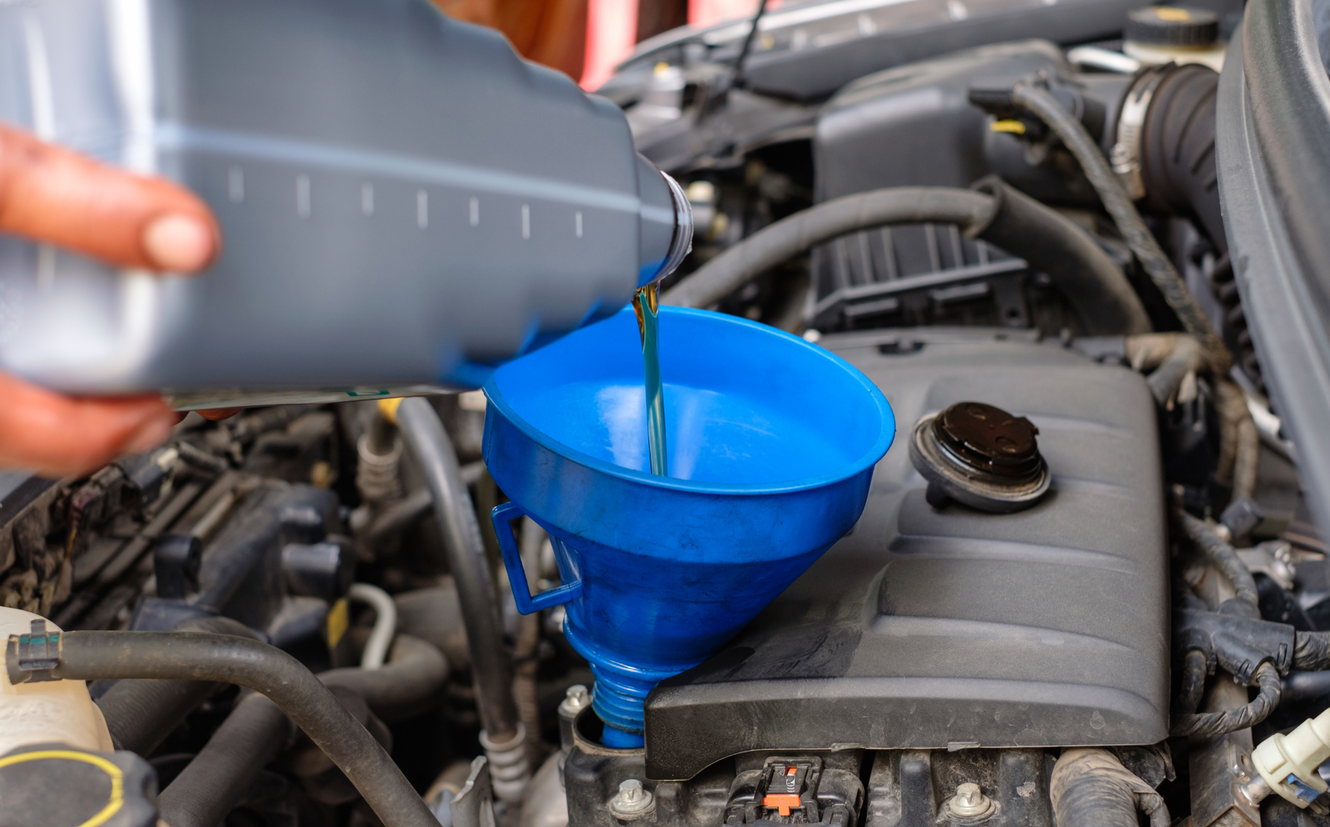 Oil being poured from a bottle into a blue funnel in a car engine bay