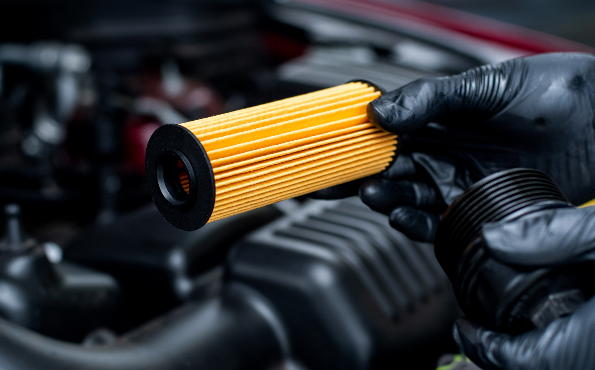 Gloved hands holding a yellow car engine oil filter near an open engine compartment