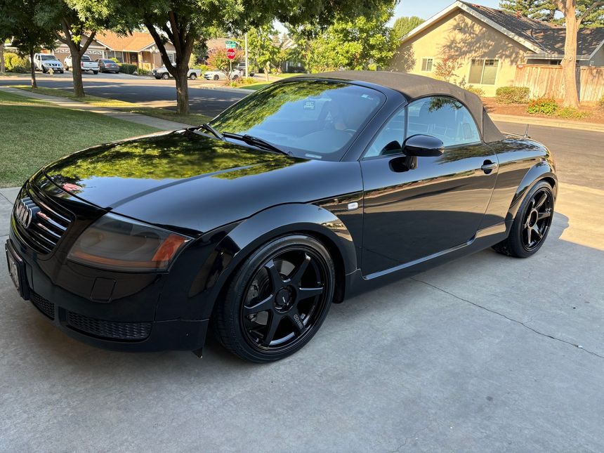 Black convertible sports car parked in a driveway on a sunny suburban street