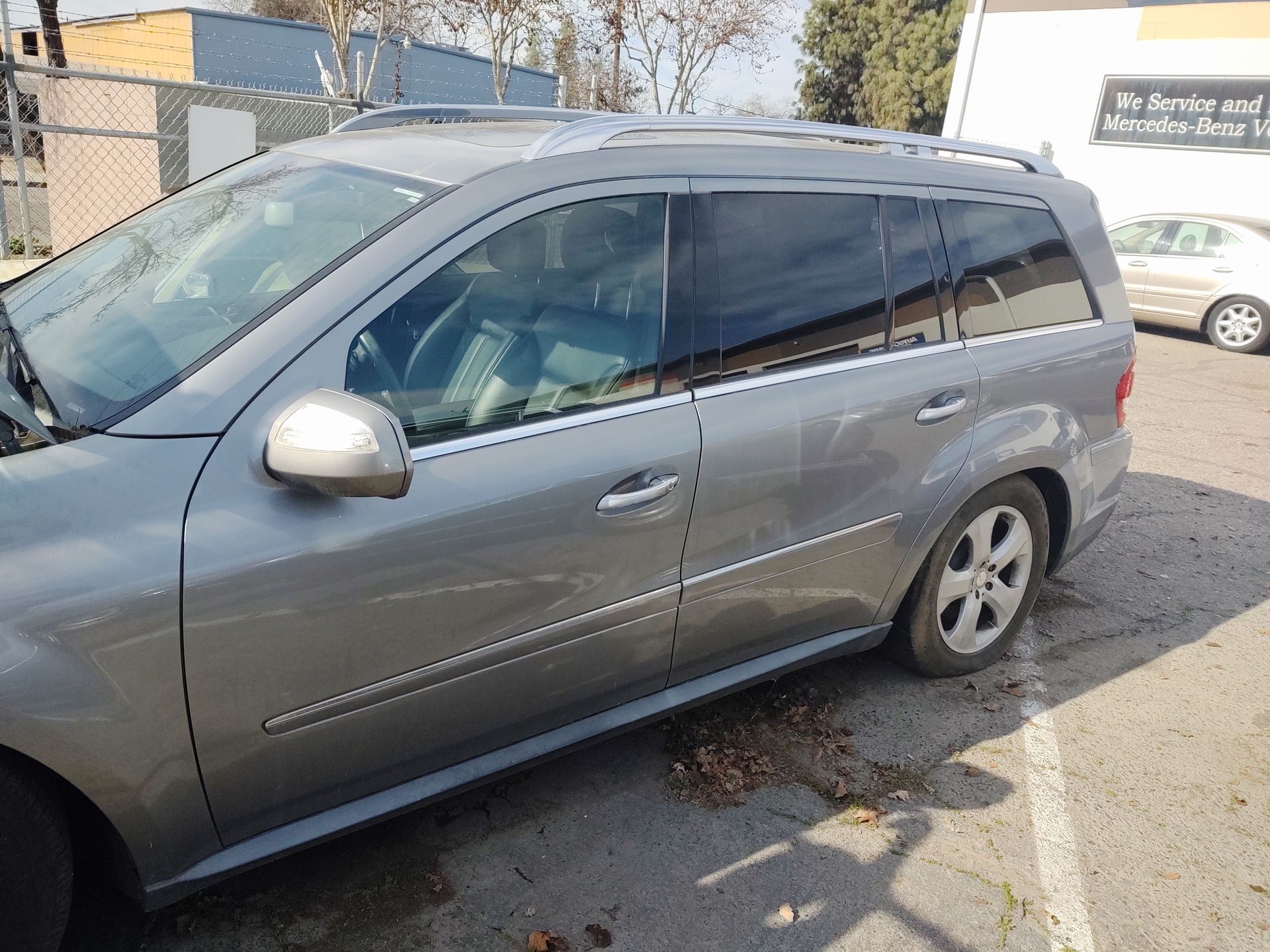 Gray minivan parked outdoors beside a fence on a sunny day