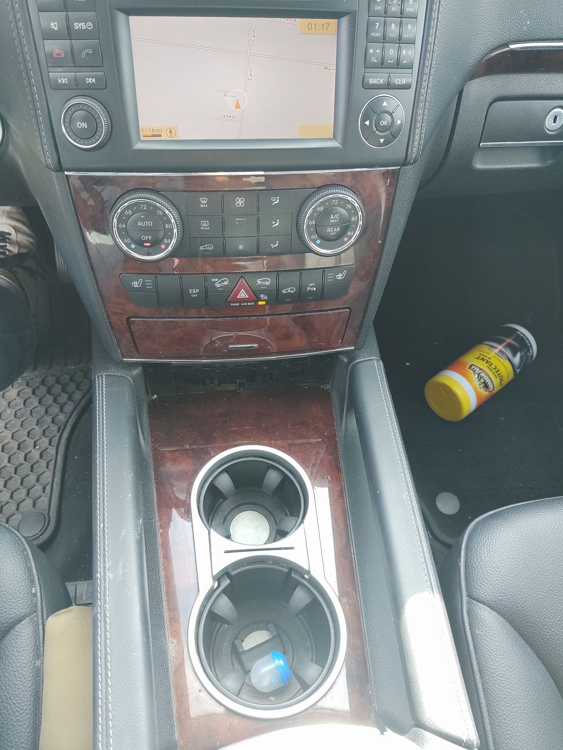Car dashboard with navigation screen, wood trim, cup holders, and a yellow can in the passenger footwell