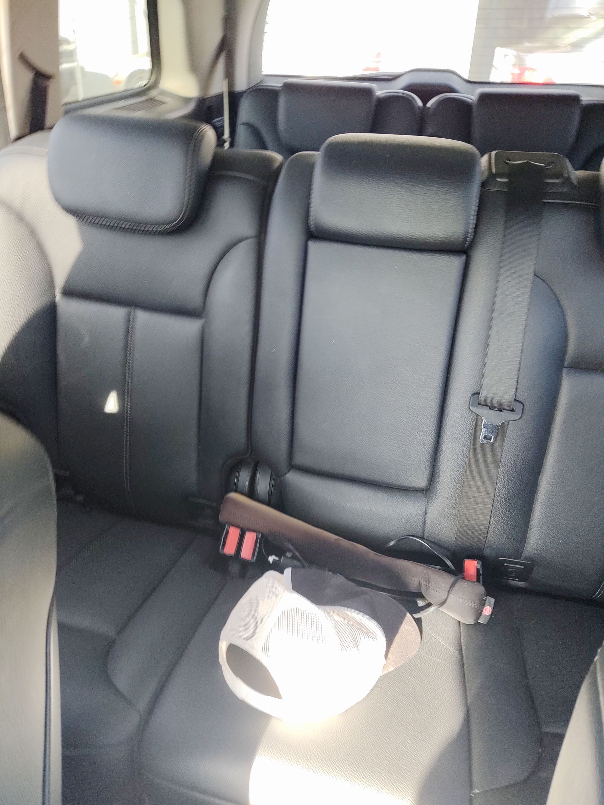 Empty black leather car back seat with a white bag on the seat and sunlight on the floor area