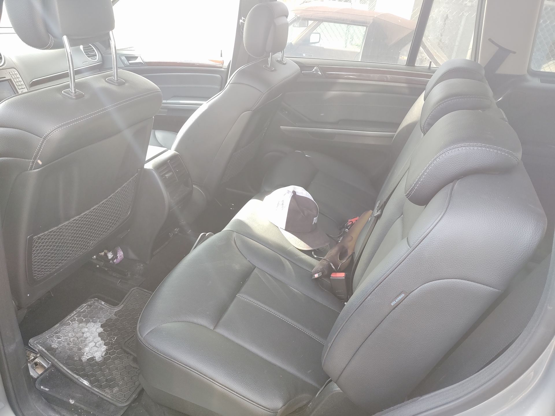 Car interior with black leather seats and debris on the floor, viewed from the back seat