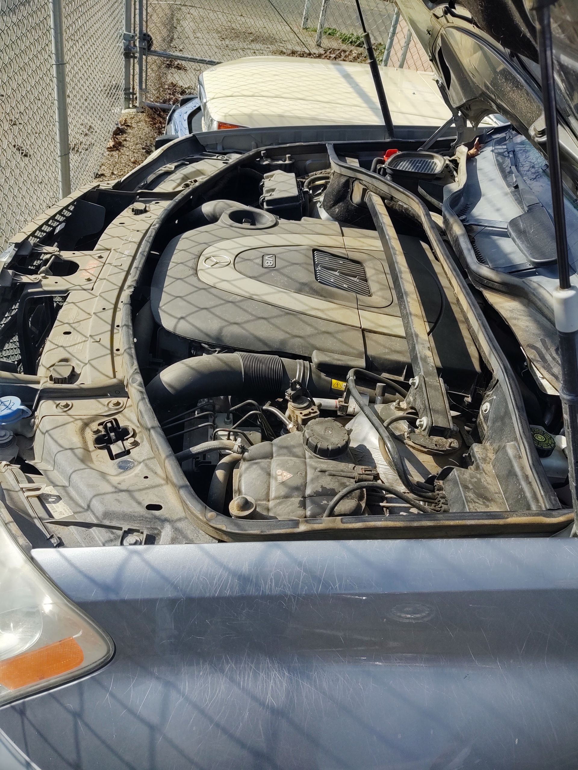 Open car engine bay with missing hood, showing dusty engine parts in a wrecked vehicle.