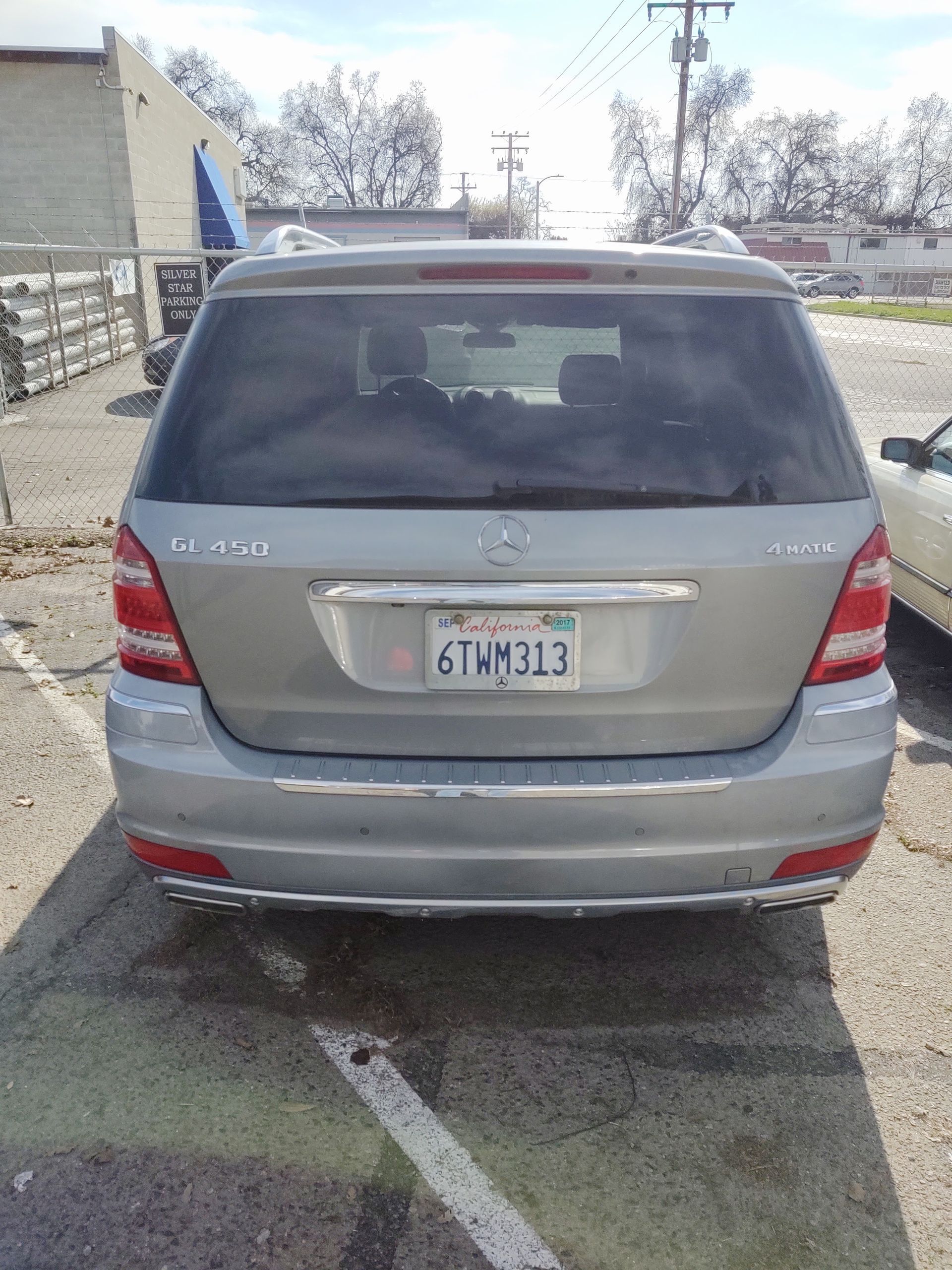 Silver SUV parked in a gravel lot beside a building, rear view with a visible license plate.
