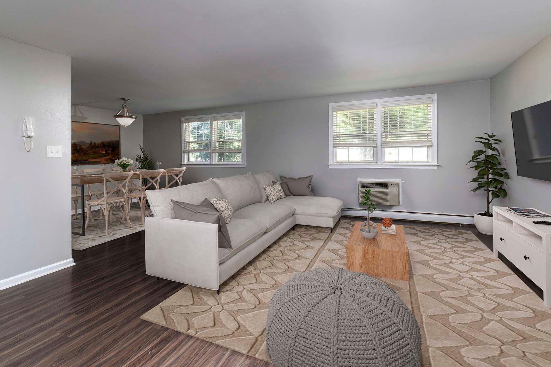 Living room in a modern apartment with a light gray palette, a sectional sofa, rug, and dining area in the back.
