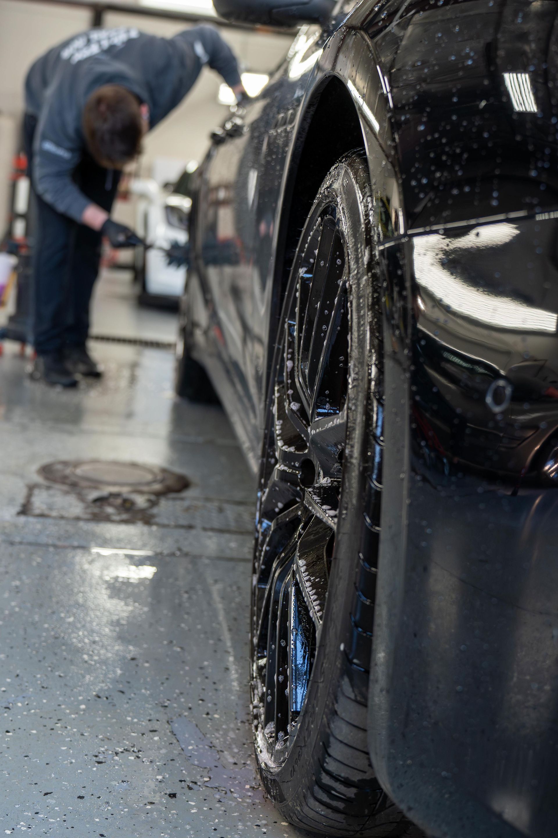 A man is washing a black car in a garage.