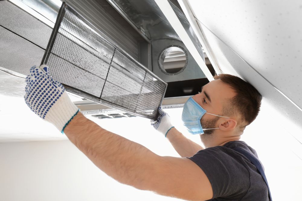 Man In Gloves And Mask Replacing An Air Filter In A Ceiling Vent — Electrical & Air Cooling Solutions in Railway Estate, QLD