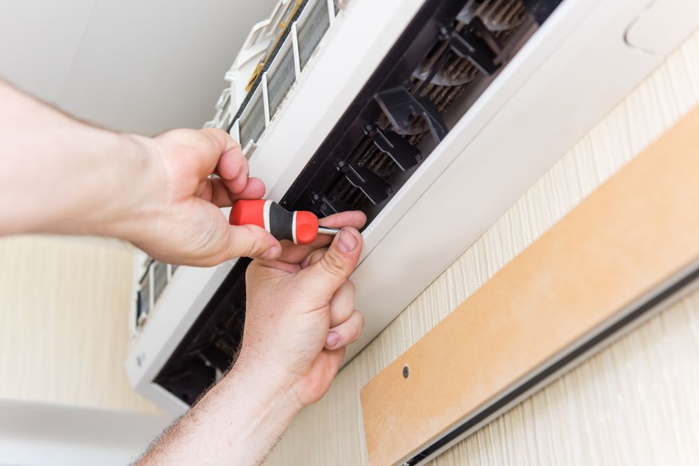 Hands Using A Screwdriver To Repair A White Air Conditioning Unit — Electrical & Air Cooling Solutions in Charters Towers, QLD