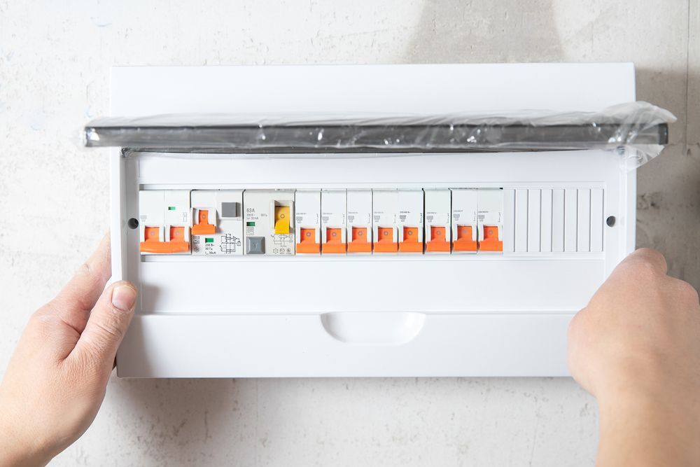 Hands Opening A White Electrical Breaker Box With Orange Switches — Electrical & Air Cooling Solutions in Charters Towers, QLD