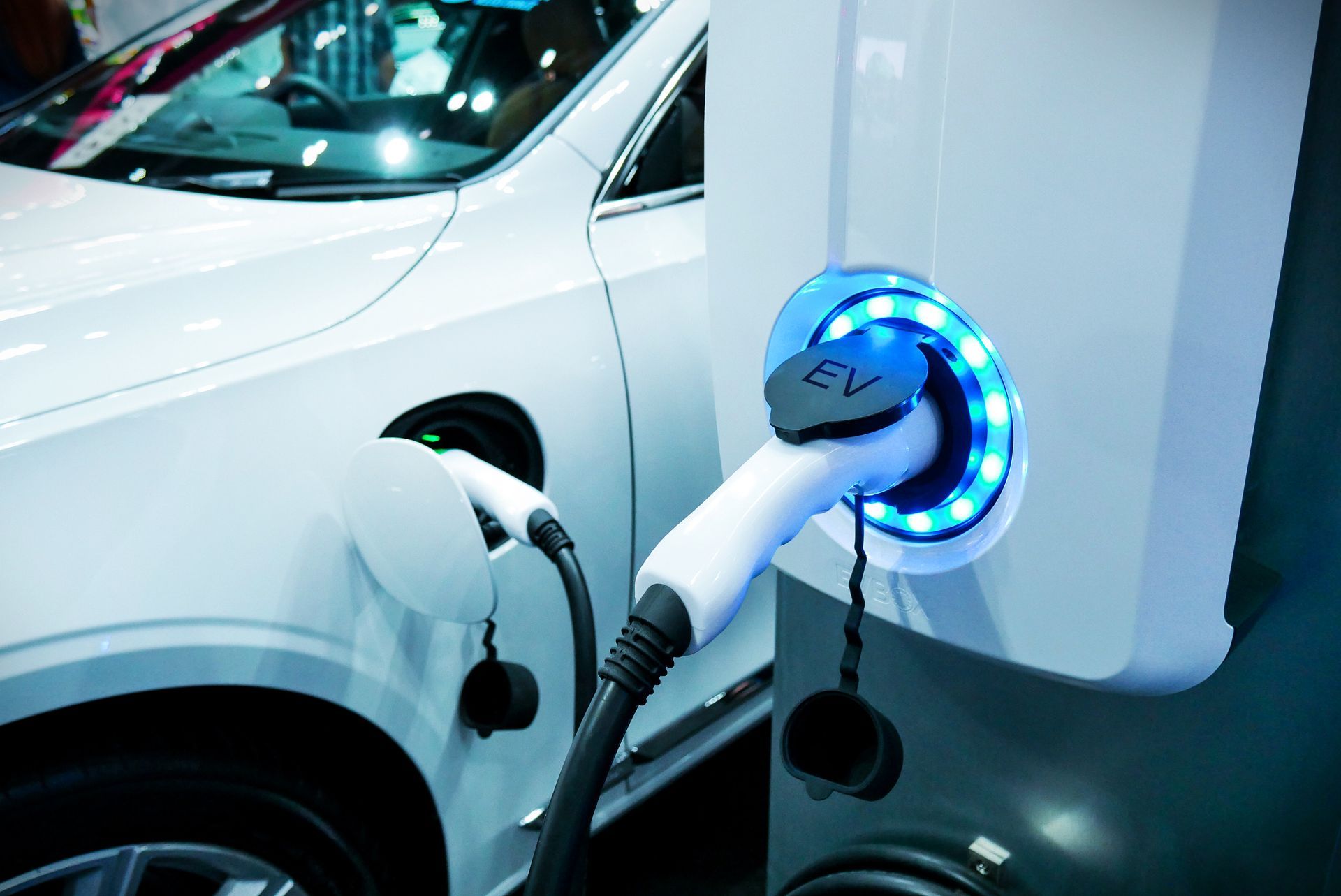 Voiture électrique blanche en charge sur une borne de recharge blanche avec des lumières bleues.