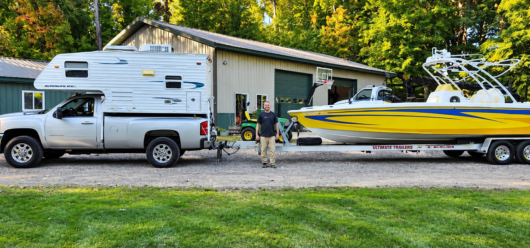 Pickup truck towing a camper and yellow speedboat beside a small building in a grassy lot