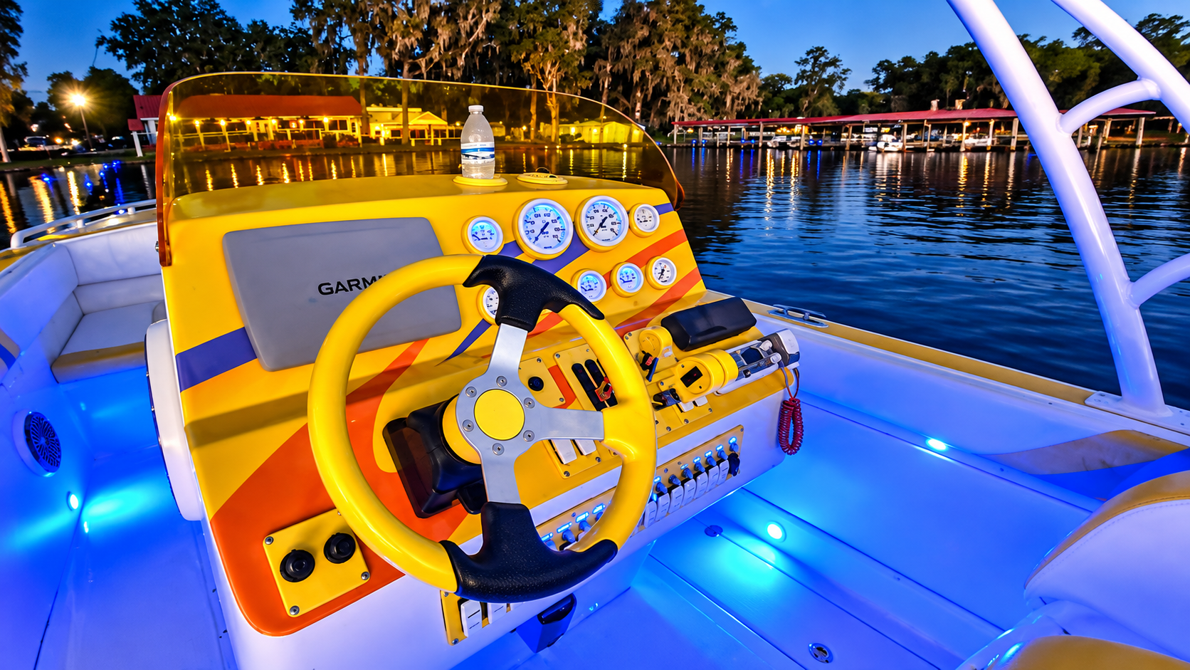 Bright yellow boat helm with steering wheel and gauges on a lit deck at dusk over water