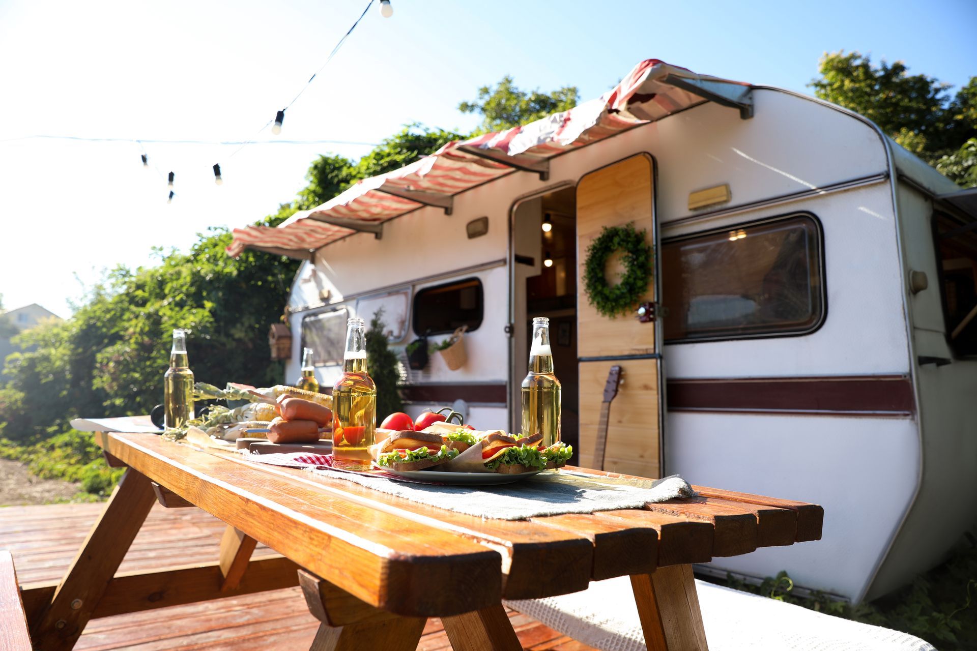 Camper van with open awning beside a picnic table set with food in a sunny outdoor campsite