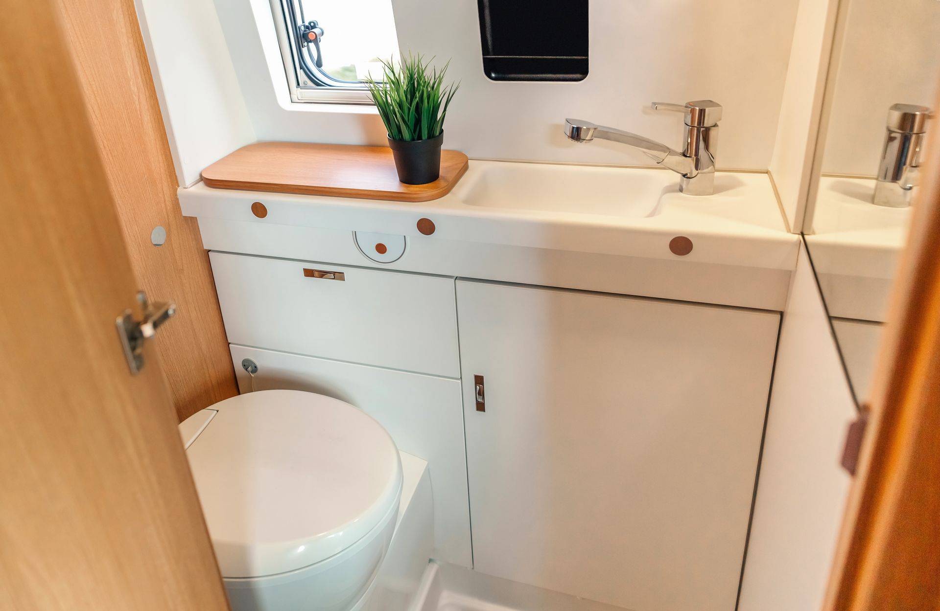 Small bathroom with toilet, sink cabinet, and potted plant on the vanity by a window.