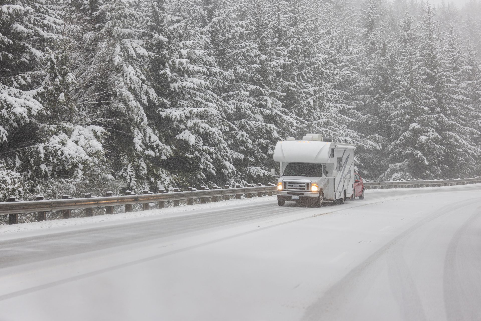Truck driving on a snowy highway beside snow-covered pine trees