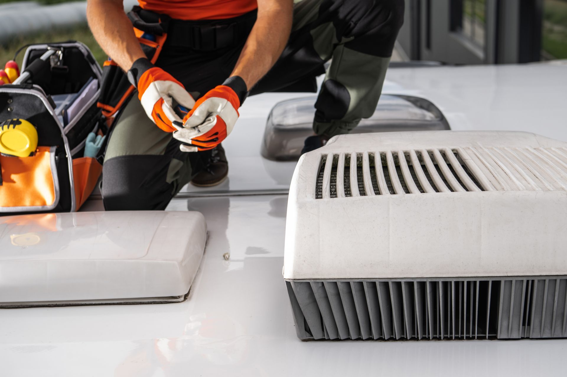 Technician cleaning a rooftop HVAC unit with tools beside a gray vented unit