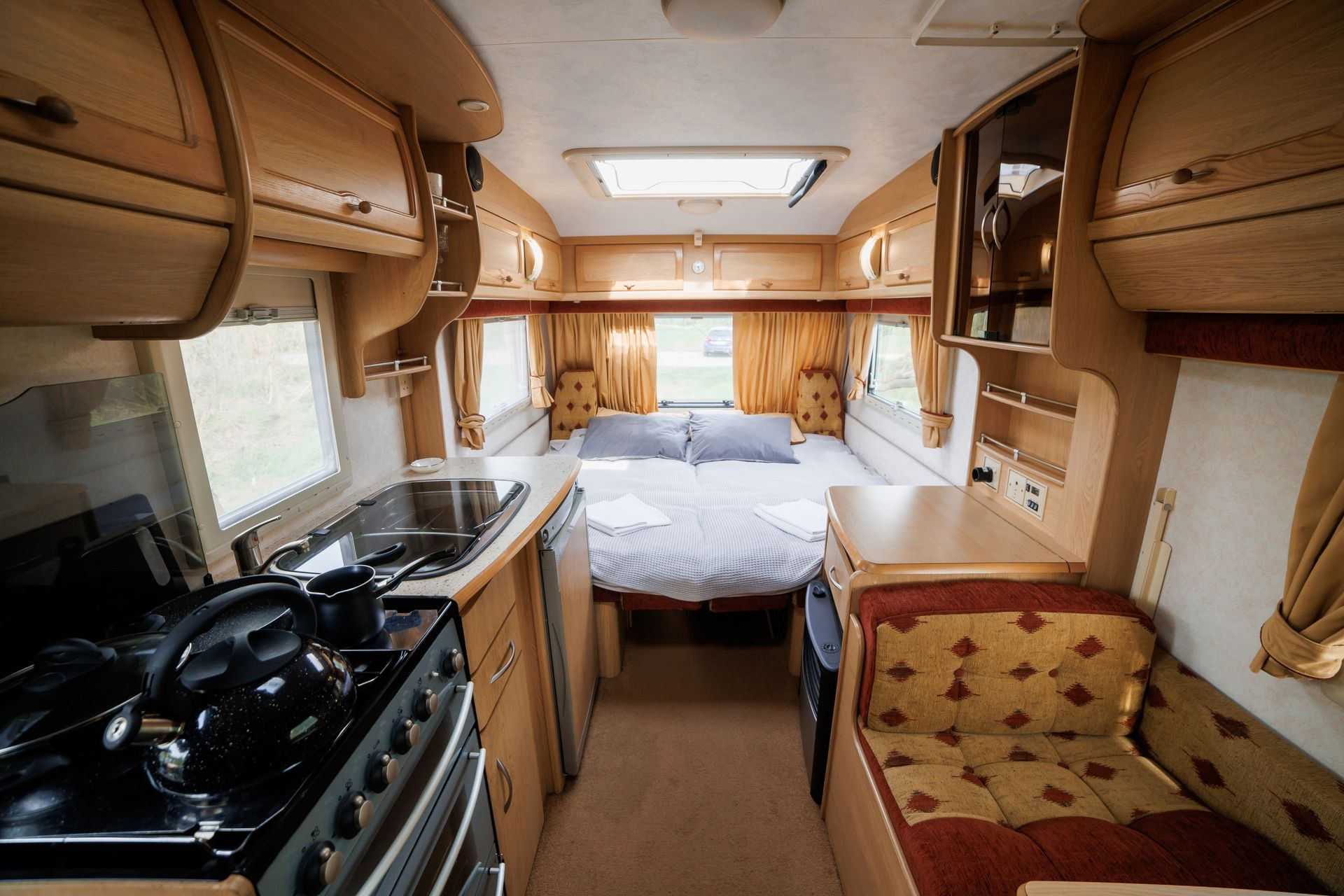 Compact RV interior with a bed at the back, kitchenette on the left, and cushioned seating on the right.