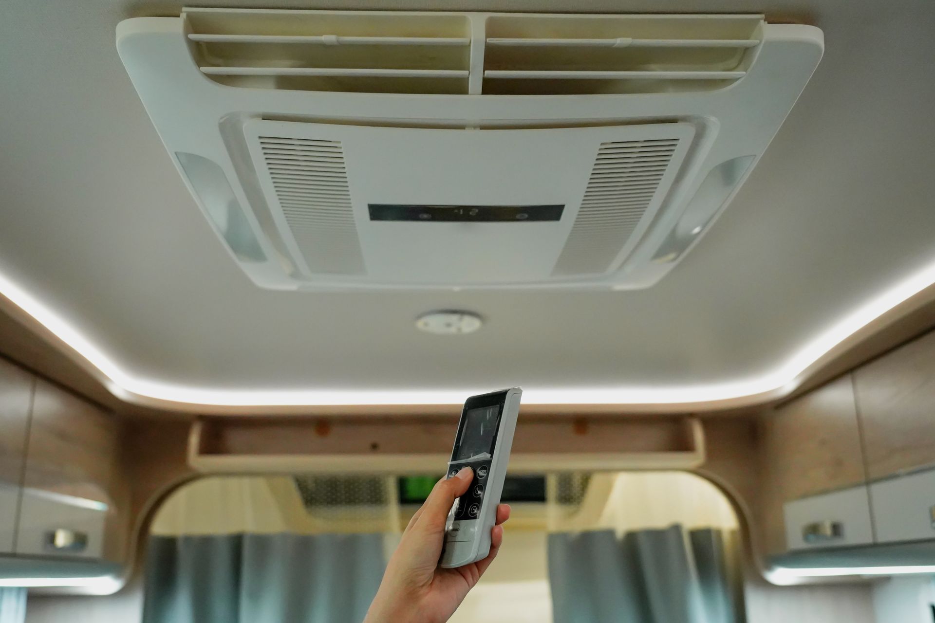 Hand holding a remote pointed at a ceiling air conditioner inside a RV