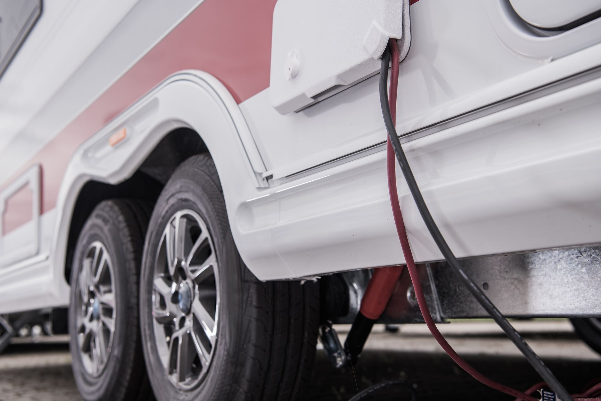 RV wheels with a red power cable plugged into the side of a white and pink camper