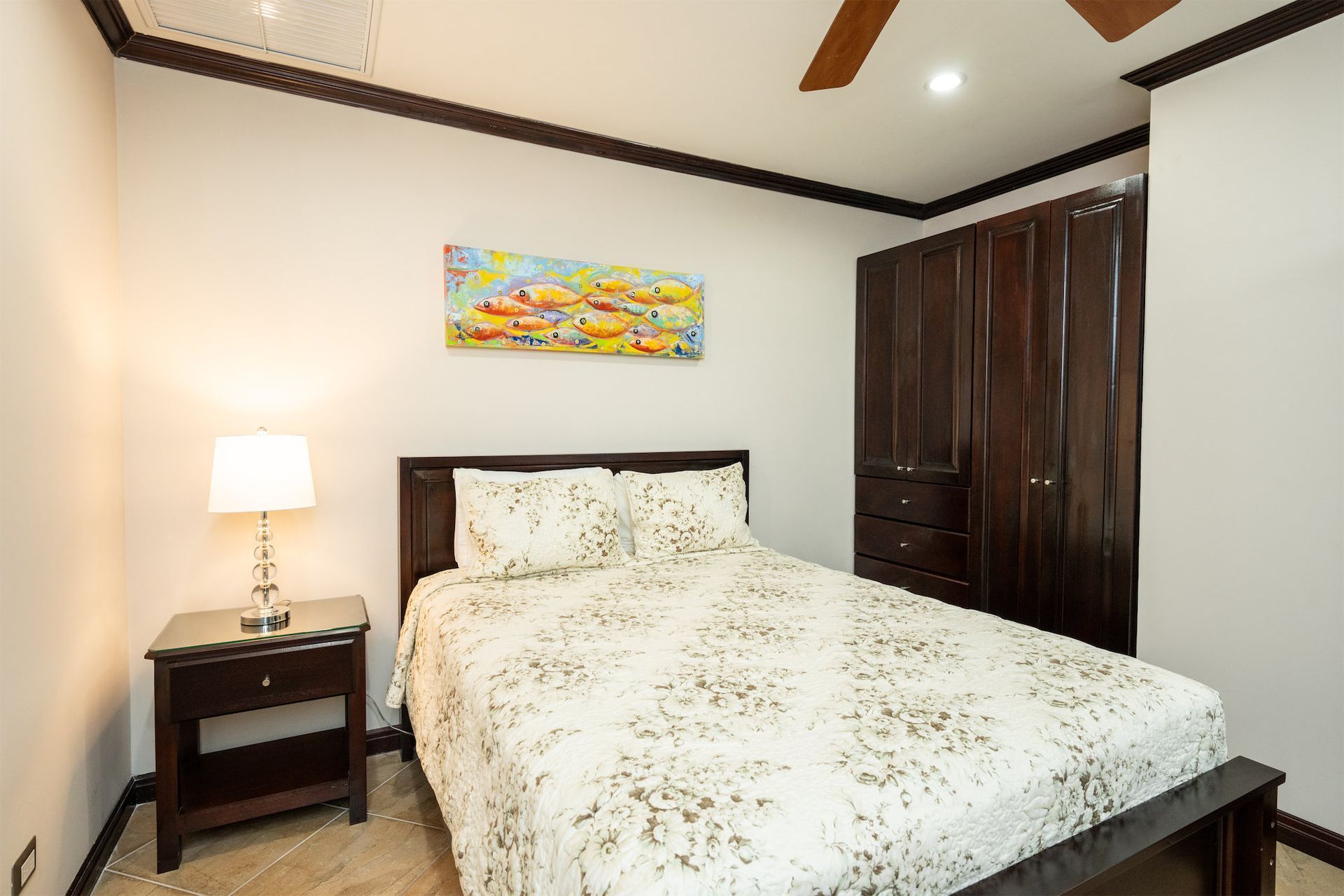 A bedroom with a bed , nightstand , lamp and ceiling fan