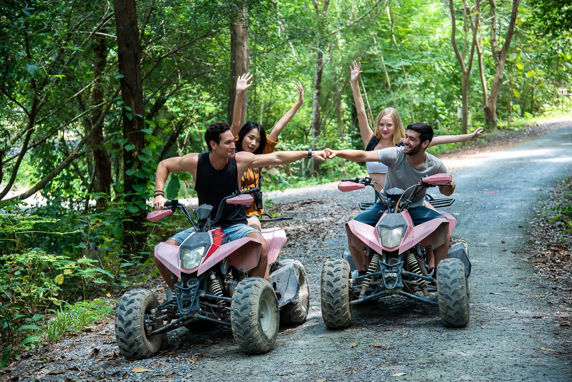 A group of people are riding atvs down a dirt road in the woods.