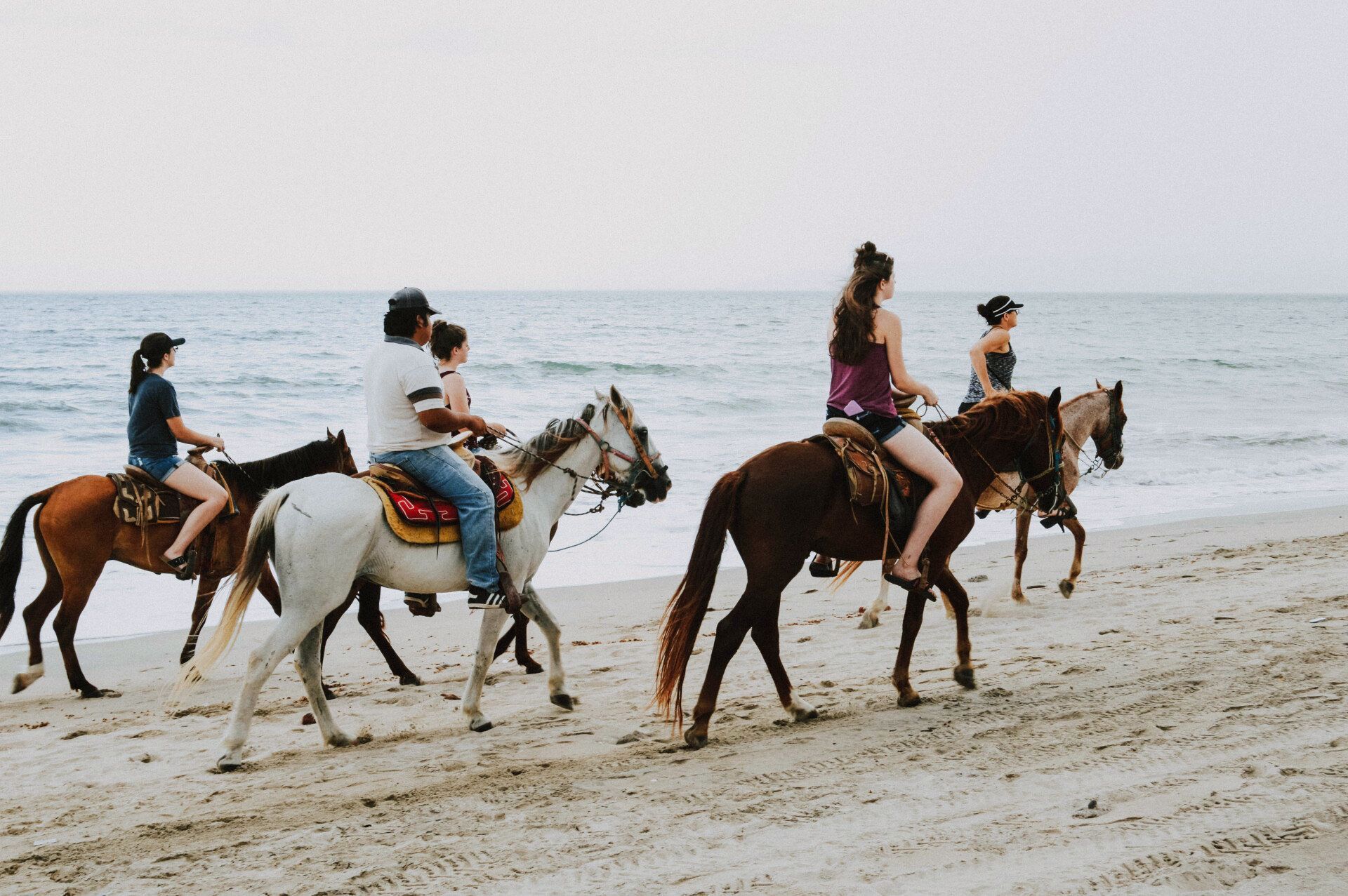 A group of people are riding horses on the beach