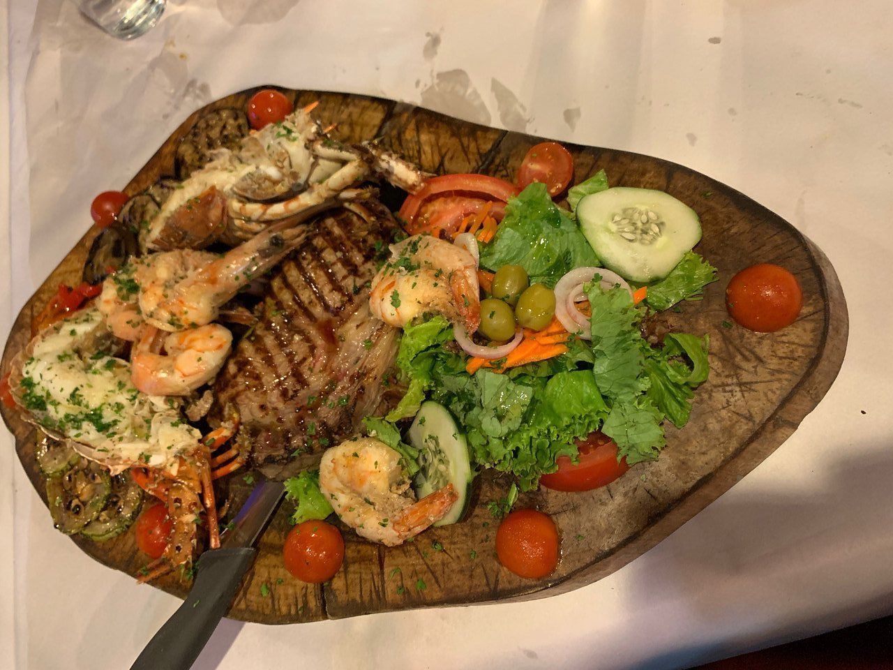 A plate of food with meat , shrimp , and vegetables on a table.
