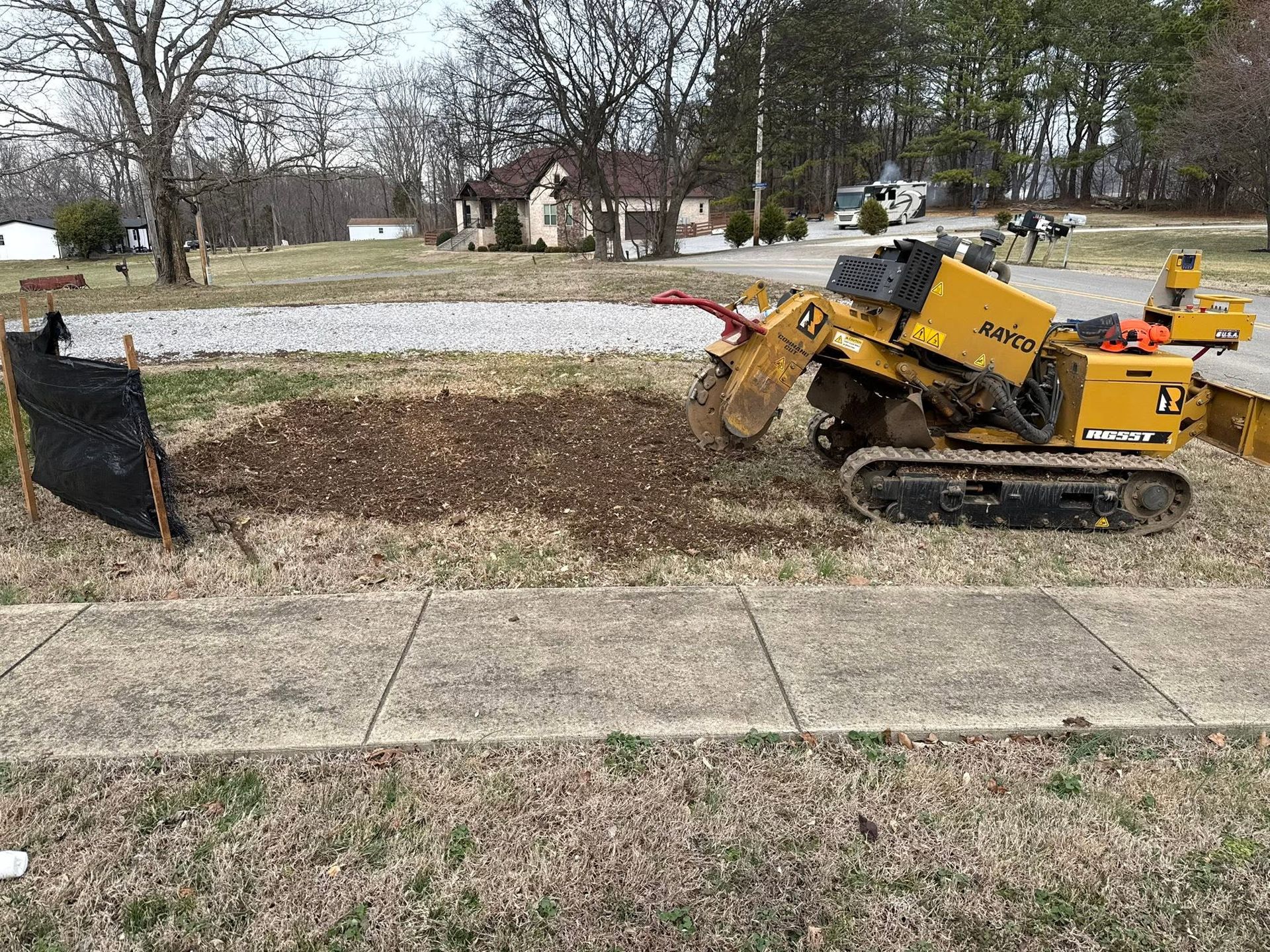 Yellow excavator digging along a roadside beside a sidewalk and gravel area.