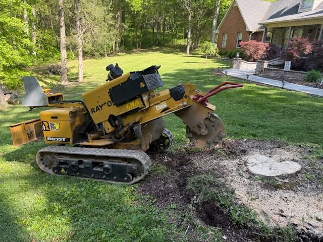 Yellow tracked stump grinder chewing up a tree stump in a grassy yard beside a house