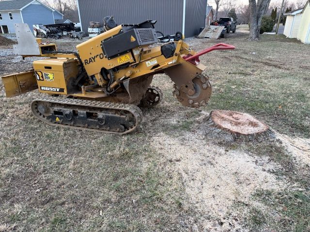 Yellow tracked trencher on a grassy yard, digging near a house with a raised soil pile.