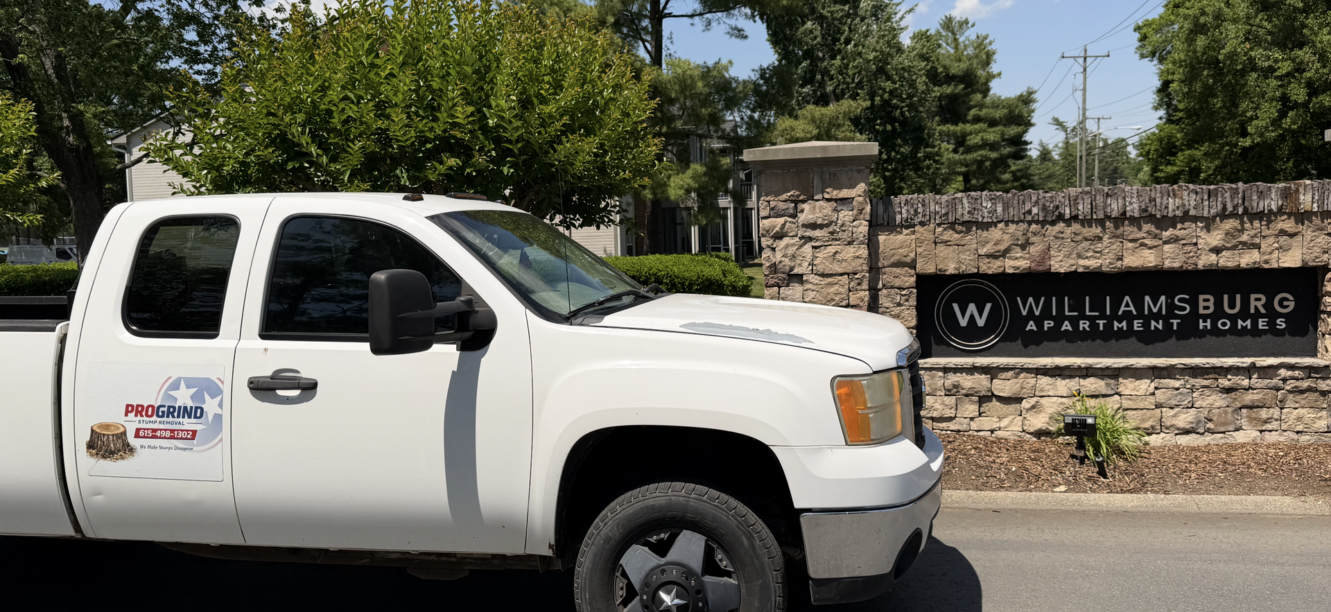 White pickup truck parked by a Williamsburg sign and stone wall on a sunny day