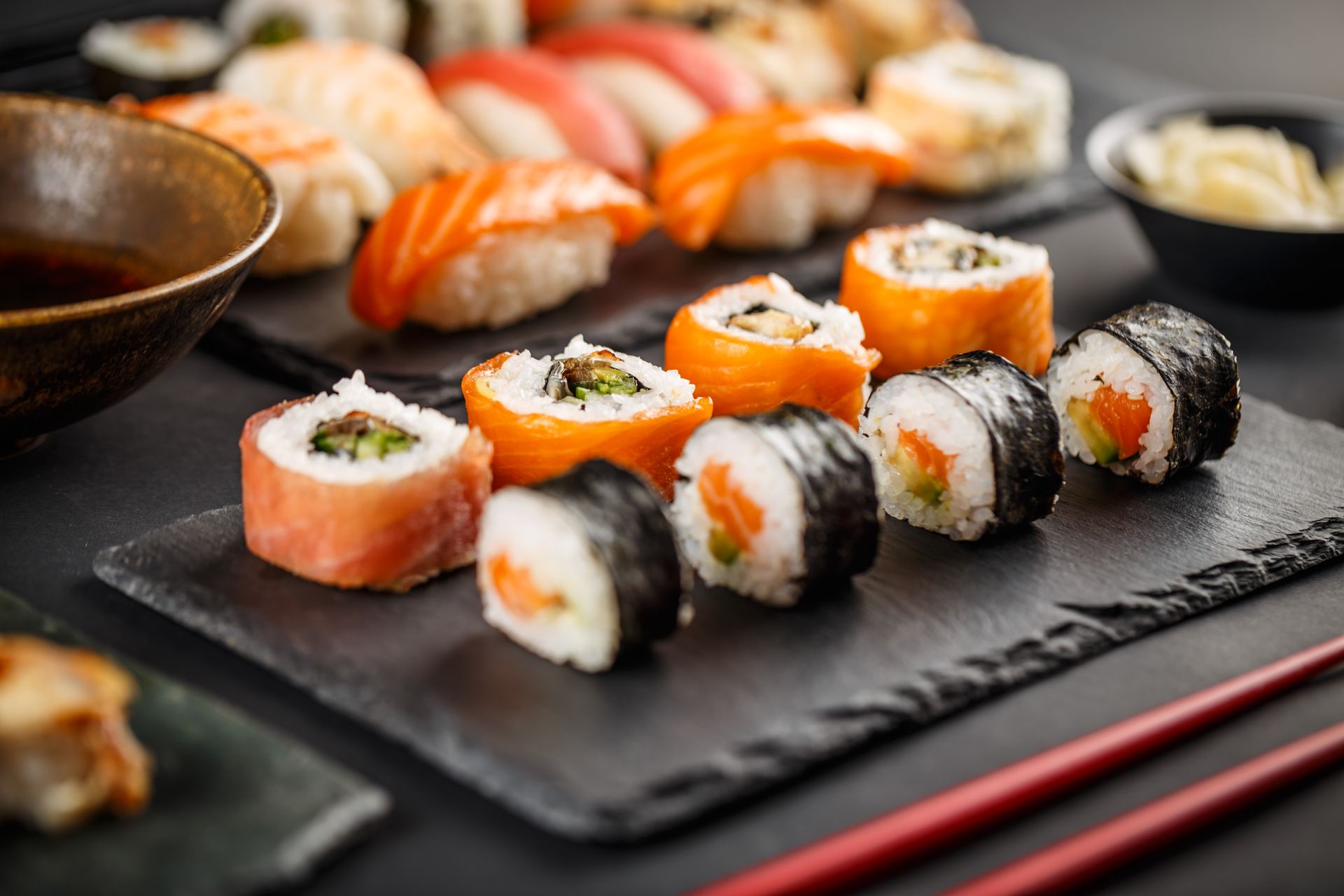 Assorted sushi rolls and nigiri on a black slate plate with chopsticks and soy sauce
