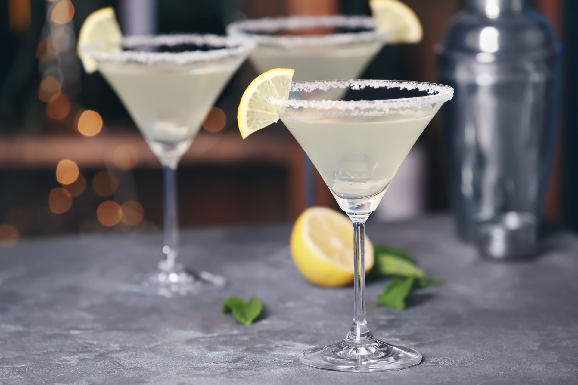 Two lemon martinis with sugared rims on a bar counter, one garnished with a lemon slice