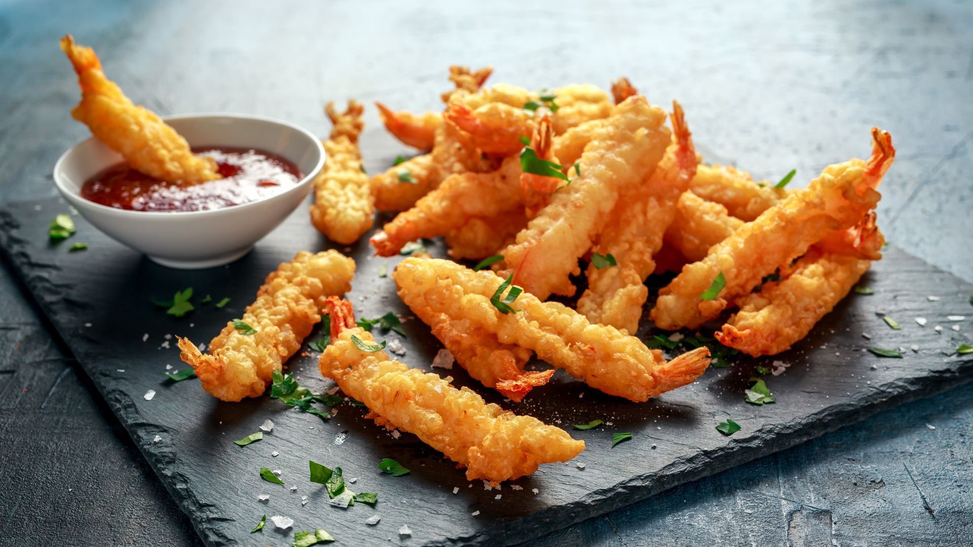 Crispy fried shrimp on a dark slate plate with dipping sauce and parsley garnish