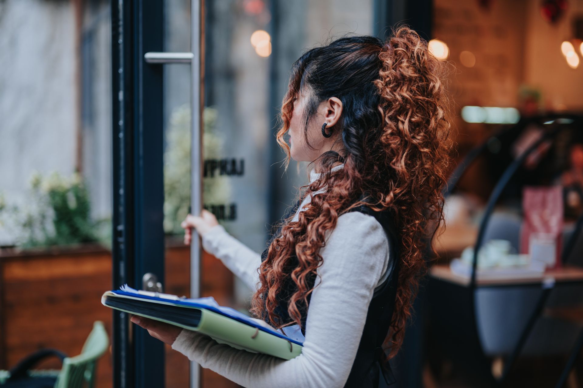 Person with curly hair holding a clipboard outside a storefront window