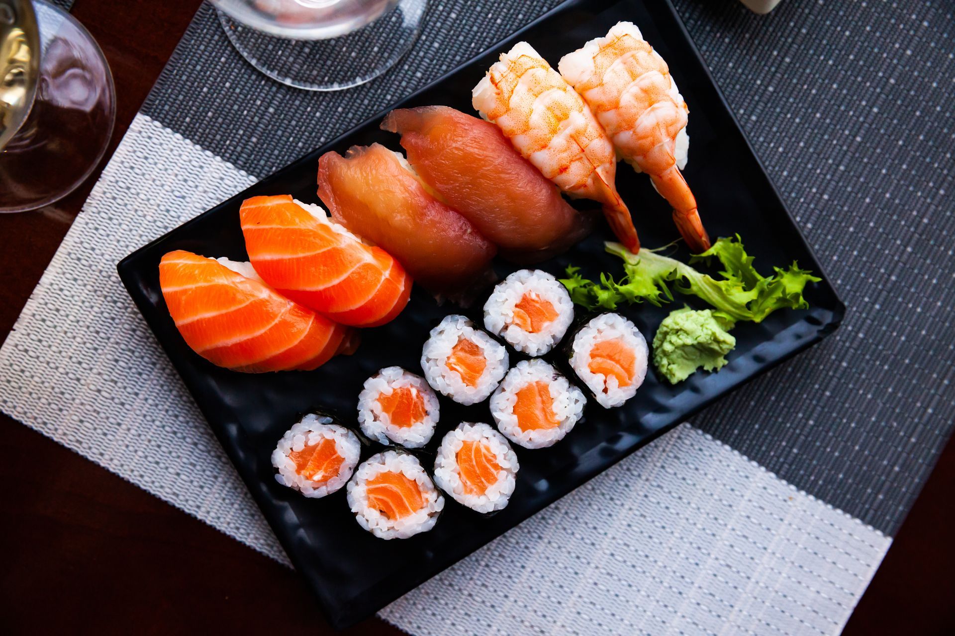 Sushi platter on a black plate with salmon nigiri, rolls, and sashimi on a table
