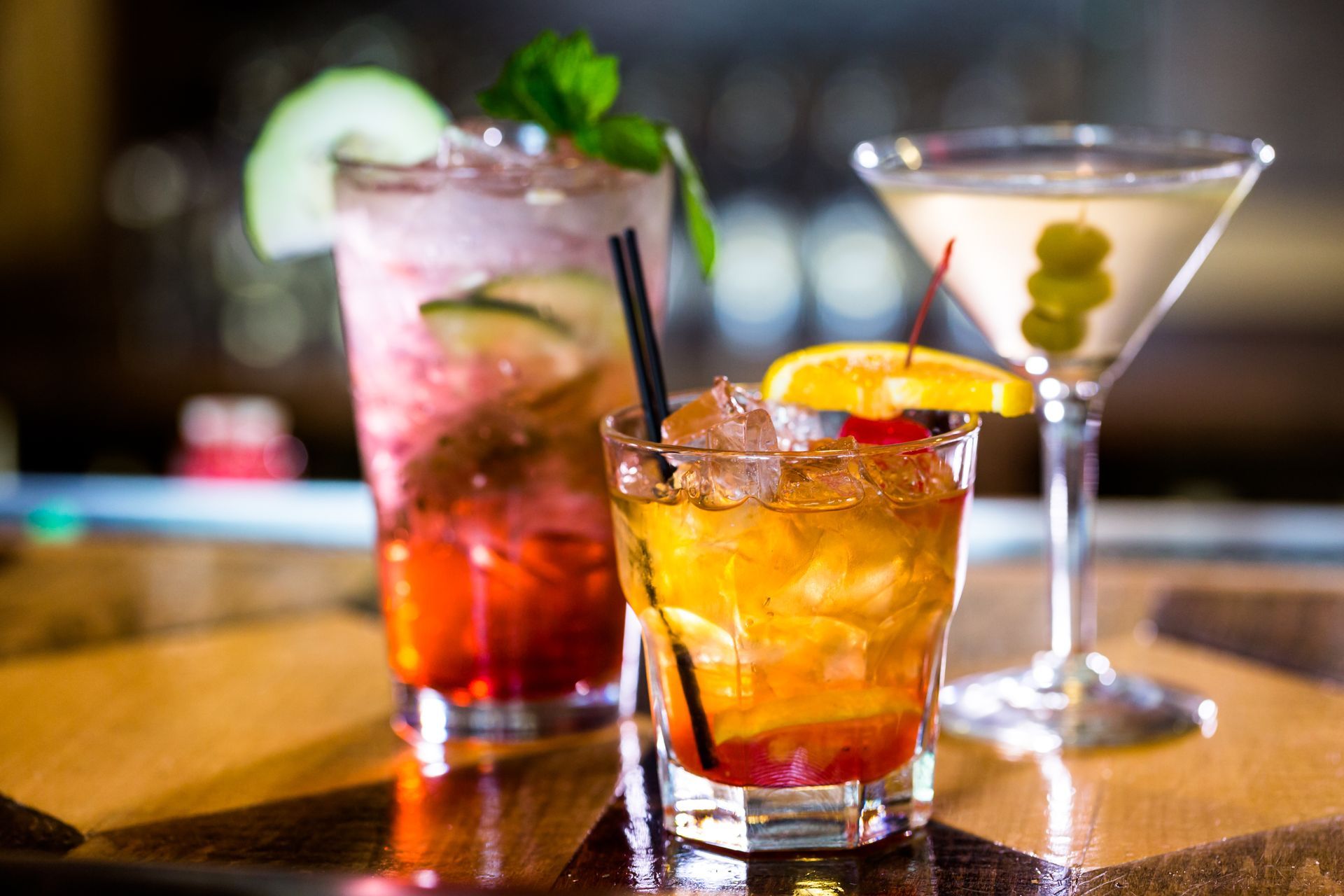 Three colorful cocktails with ice, citrus, and mint on a bar counter