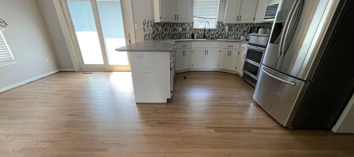 An empty kitchen with hardwood floors and stainless steel appliances.