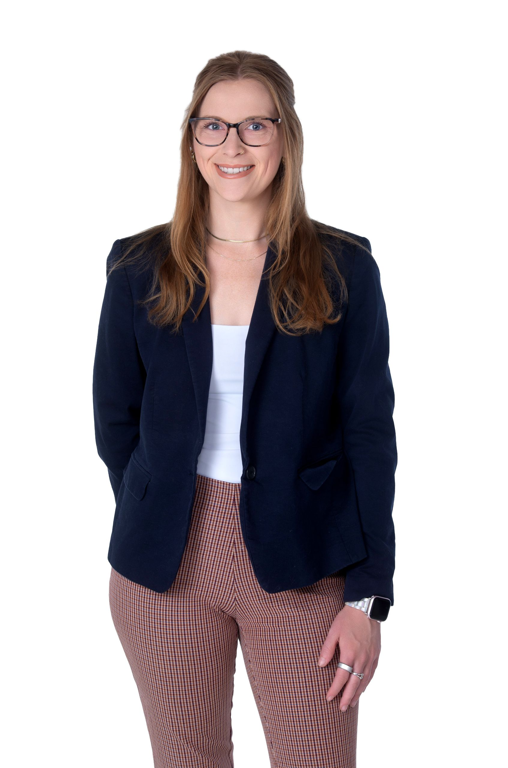 Person standing against a white background, wearing a navy blazer, white top, and patterned pants.