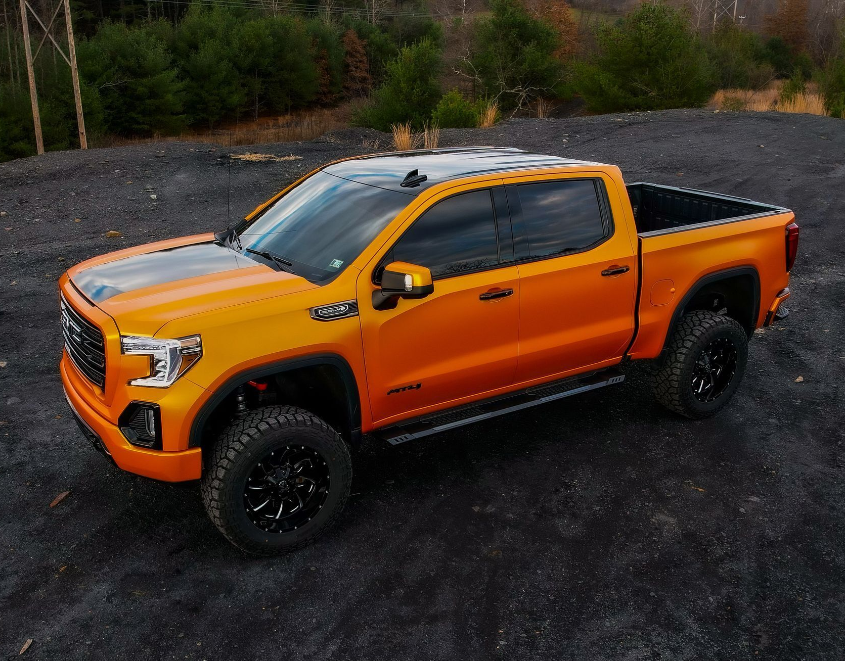 Orange GMC truck with black accents, parked on gravel.