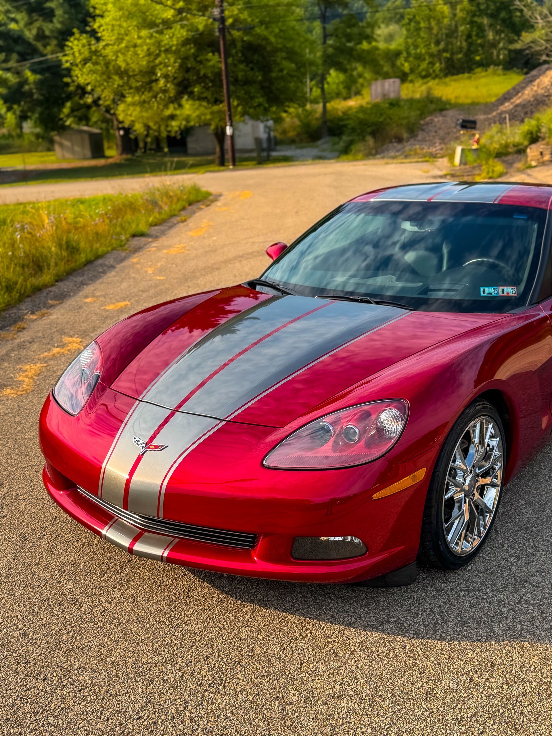 Red Corvette sports car with silver racing stripes parked on a gravel road.